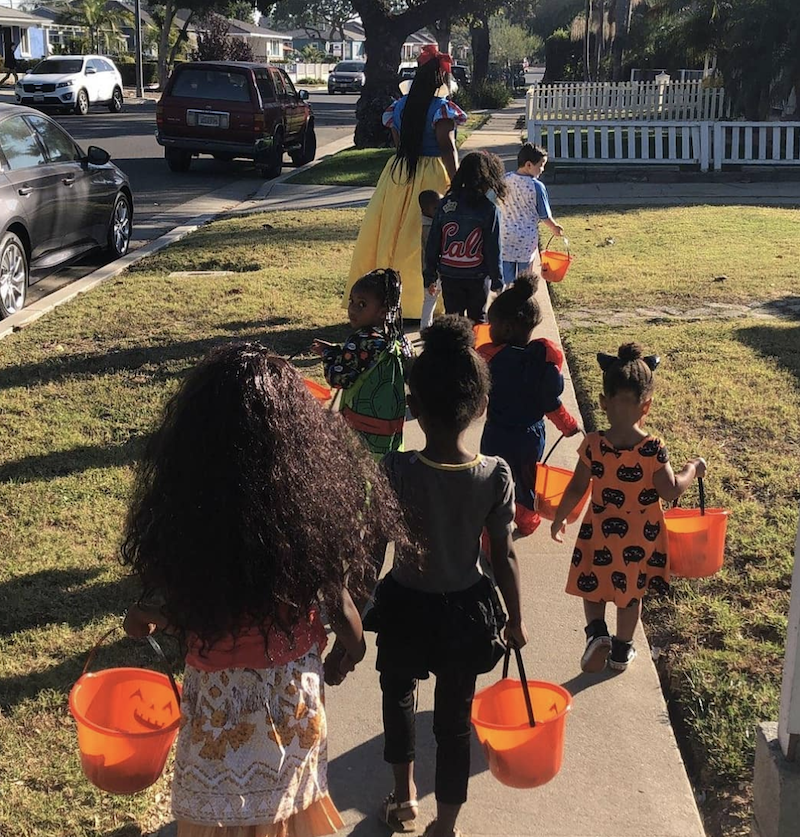 Children are dressed up in costumes for Halloween carrying candy baskets.