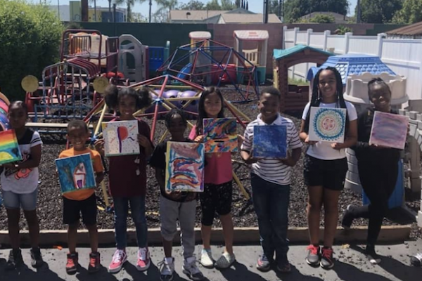 Proud children are smiling, holding up their painting, and taking a picture.